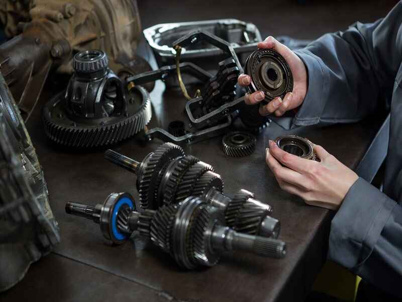 "A mechanic assembling gear components on a workbench, with various mechanical parts, gears, and shafts, representing the detailed process of maintenance and installation in mechanical systems."