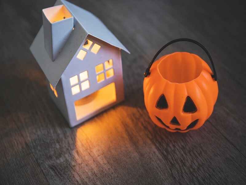 "Minimalist Halloween background featuring a small glowing house lantern and a carved pumpkin bucket on a wooden surface, symbolizing a cozy yet spooky Halloween atmosphere." 