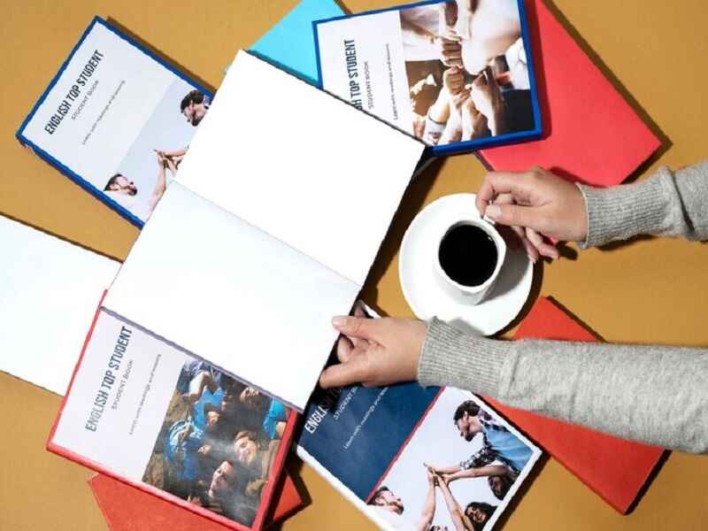 "Person reading an English textbook with multiple study guides arranged on the table, symbolizing a focus on education, language learning, and academic preparation." 