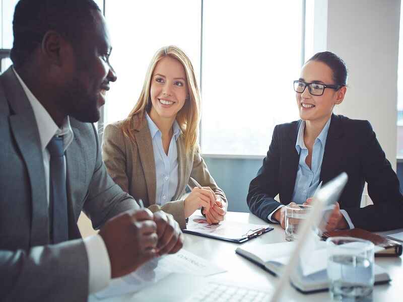 The alt text for the image could be: "Business professionals engaged in a discussion at a meeting, smiling and collaborating around a table.