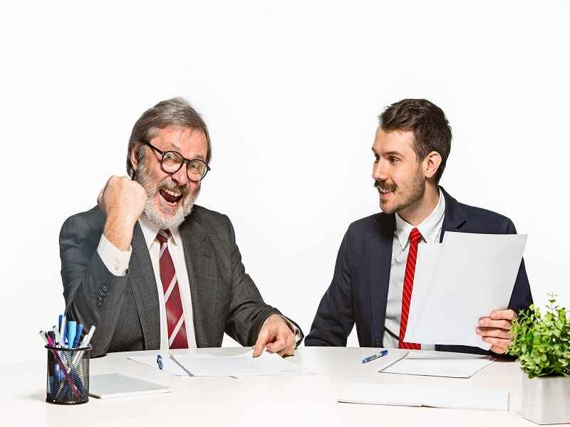 "Two business professionals celebrating a successful deal, with one man cheering in excitement and the other smiling while holding documents. Represents successful negotiations, partnerships, or corporate achievements." 