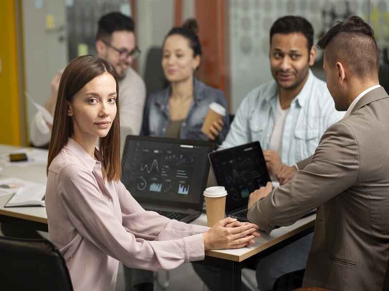 "A group of employees working together in a modern office, using laptops with data charts on the screens, representing team collaboration and the use of AI tools for tracking team performance and improving communication." 